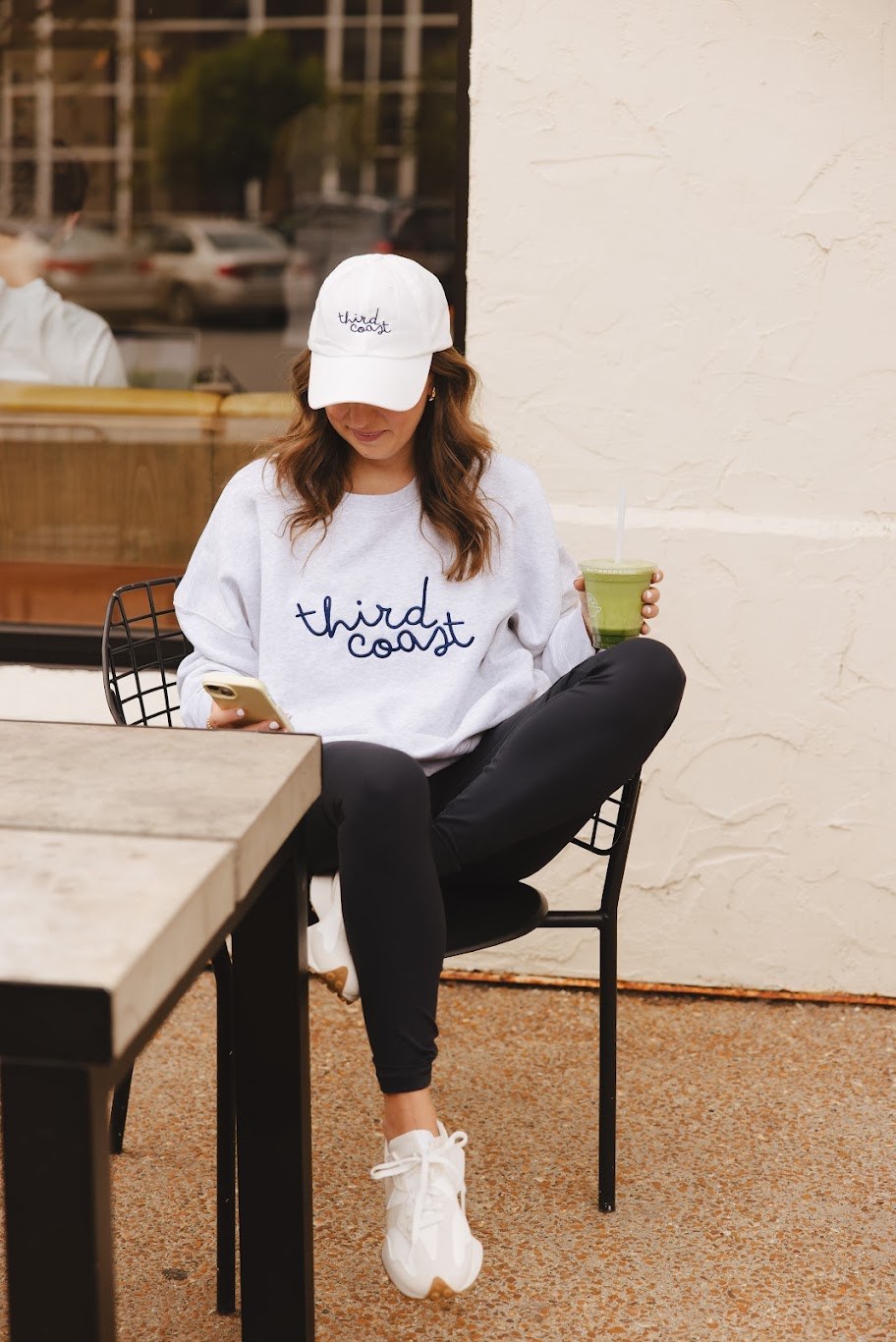 The Third Coast script crewneck and cap in white, worn at a coffee shop